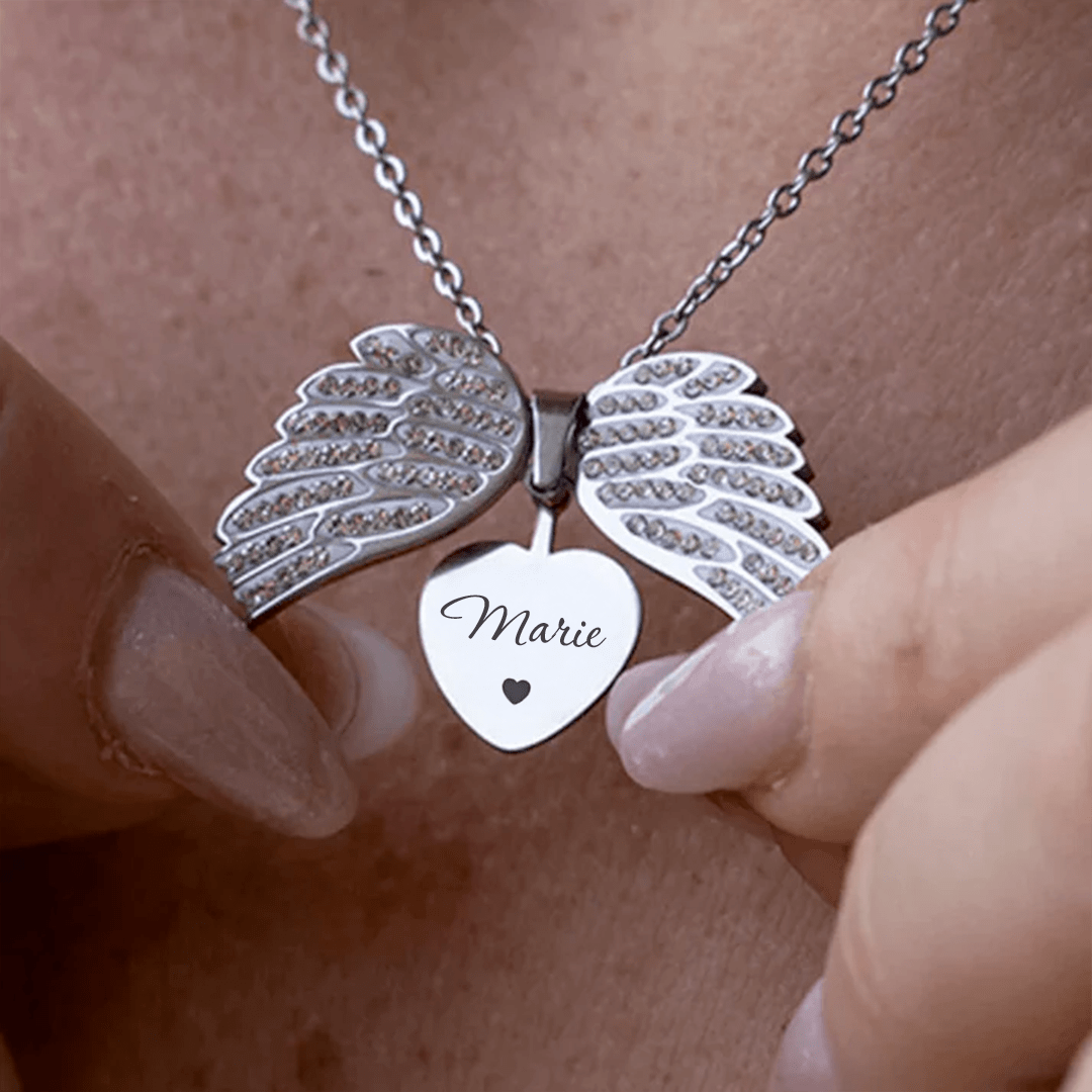 ORLA silver heart pendant engraved with 'Marie', angel wings open, held in hand on chain