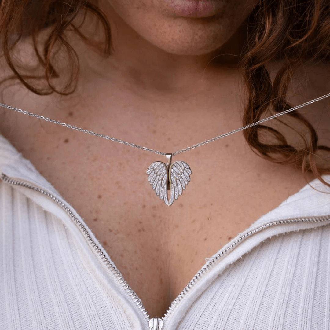 Silver Eternal Embrace Heart Pendant with angel wings by ORLA, shown with woman in background.